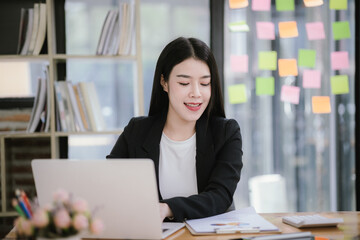 Image of Asian businesswoman working with laptop in home office. Beautiful woman sitting at desk, laptop, smartphone and documents on table.