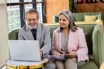 Executive discussing with senior professional while working on laptop at office