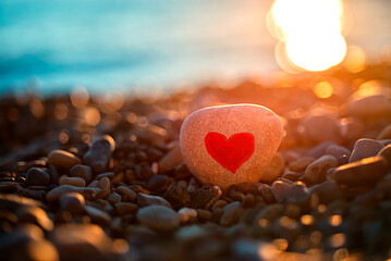 Fototapeta premium Red heart on a stone on the seashore against the backdrop of sunset. Valentine's Day