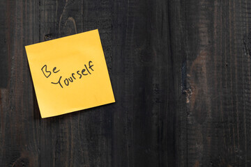 Positive idea concept image using a wooden table and a sticky note with the words Be yourself