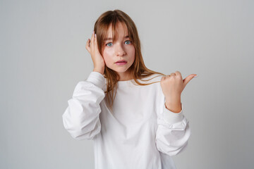 Young girl happily pointing against a neutral background while wearing a cozy white sweatshirt