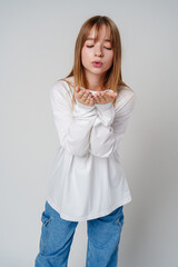 Young woman in white long-sleeve shirt blowing a kiss against a plain background