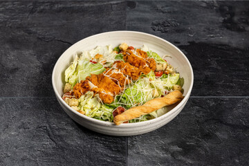 Caesar Salad with Fried Chicken Strips and Breadstick on dark stone background
