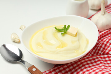 Mashed potatoes in bowl on towel, spoon and garlic on white background, close up
