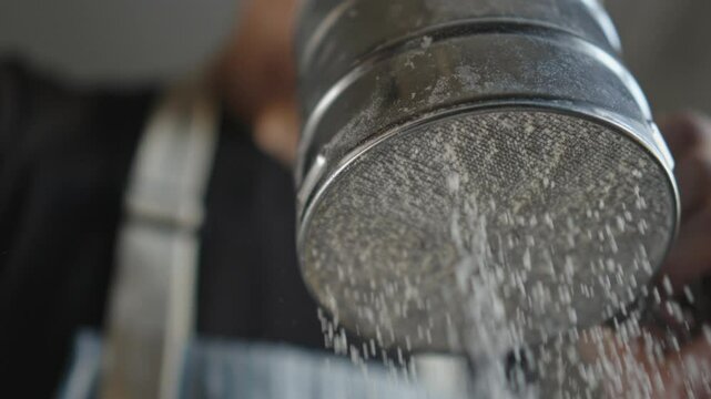 A male chef in the process of sifting white wheat flour with a sieve for making pastries or other dough products.