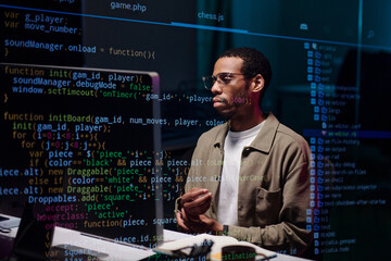 Young African American man studying programming code on a monitor in a work environment. Engaged in software development, using technology for coding projects