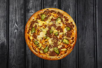 Hunter's pizza with minced meat, pickles and cheese, top view, on black wooden background.