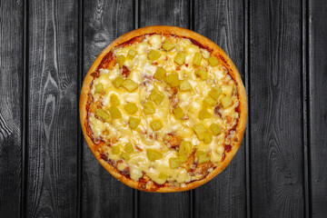 Pizza with pineapple and cheese, top view, on black wooden background.