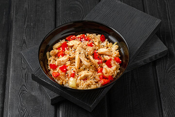 Rice with chicken and vegetables in a plate, on a black wooden background, Japanese style.