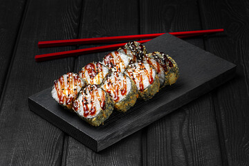 Japanese sushi, rolls fried with shrimp and teriyaki sauce on a black wooden background. Tempura roll