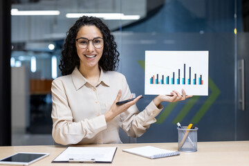 Businesswoman video call showcasing sales graph to remote team. Holding chart presenting growth....