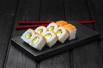 apanese sushi, rolls with salmon and bell pepper on black wooden background.