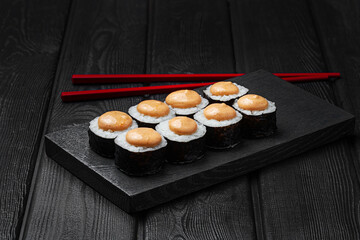 Japanese sushi rolls with cheese sauce on top on black wooden background. 