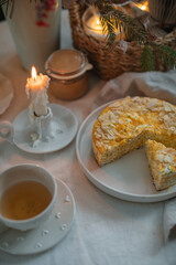 Cup of tea with a healthy cottage cheese cake with poppy seeds and almond petals on the table with a candle and Christmas decorations.