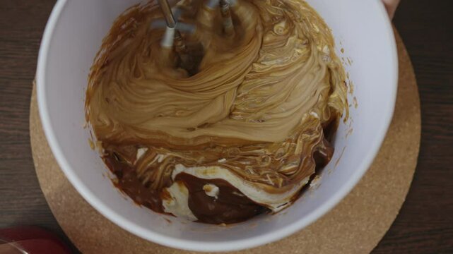 Confectioner mixes salted caramel and cream cheese. Whipping the caramel cream for the cake with a mixer. The concept of making confectionery desserts.
