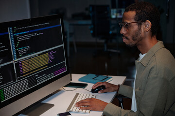 Man sitting at desk, focusing on computer monitor filled with programming code in office setting....