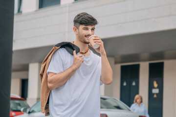 Handsome man in jacket holding paper cup on urban street