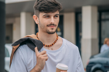 Handsome man in jacket holding paper cup on urban street