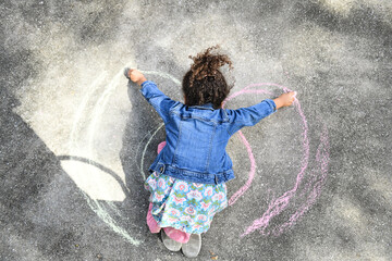 Child drawing colorful chalk rainbow on pavement, denim jacket a