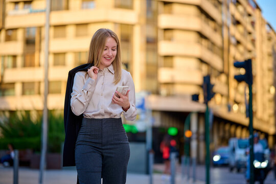 Young woman in business attire checks her phone in a city setting