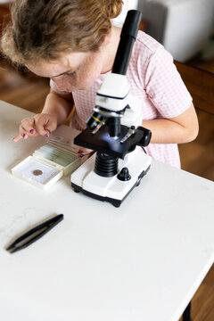 A girl with freckles examines microscope slides next to a microscope