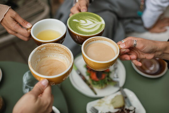 Four friends gather for breakfast and toasting with cups of coffee, buckwheat tea and matcha latte on the summer terrace.