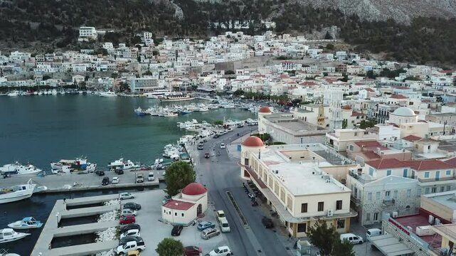 Greece,Kalimnos, Aerial footage of the city center, starting from the harbor, goes along the seaside road, flies towards to the clock tower and the church behind the iconic municipality building,