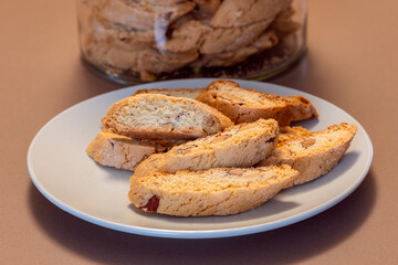 Almond cantucci cookies are arranged on a plate revealing their crisp texture and nutty flavor with a jar of similar cookies behind them ideal for enjoying with coffee or wine