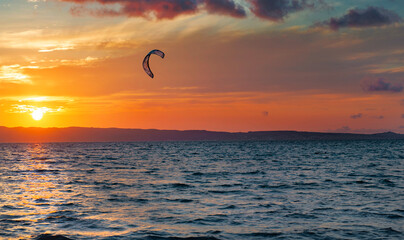 sunset over the sea with a kite surf sail under a colorful sky