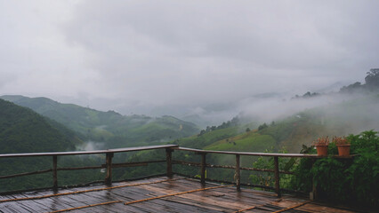 Landscape of greenery rainforest and hills outside wooden terrace on foggy day