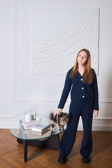 A young beautiful girl in blue clothes is standing in a loft style room with a dog in her hands