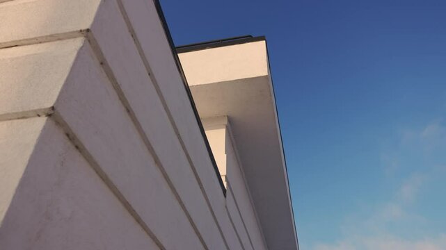 Section of facade highlighted by sunlight casting soft shadows along wall. Clean design of wall contrasts beautifully with softness of clear sky