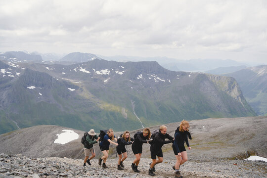 Group of friends climbing in row on mountain against cloudy sky