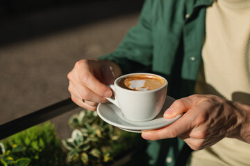 Close-up of a man sitting at an outdoor cafe drinking a delicious cappuccino on a sunny morning.
