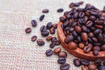 Robusta coffee beans or Coffea canephora in a wooden bowl and some scattered around it, close up view.