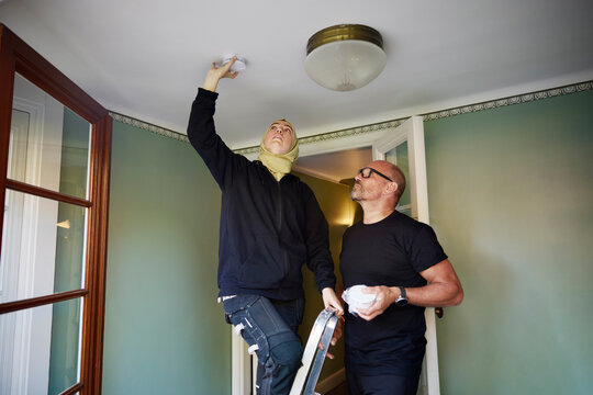 Man standing near woman installing smoke detector on ceiling at home