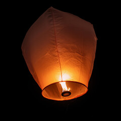 A single sky lantern isolated on black background. Rising in the dark night sky. single light in the darkness