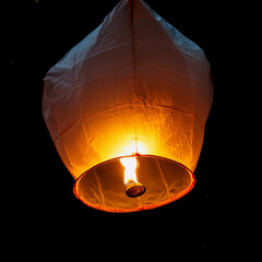 A single sky lantern isolated on black background. Rising in the dark night sky. single light in the darkness