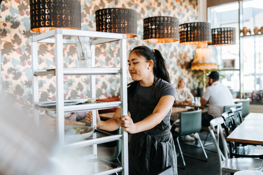 Smiling waitress pushing serving cart in cafe