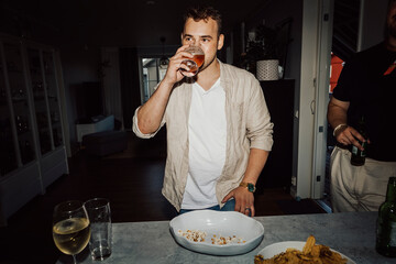 Young man drinking beer during party at home