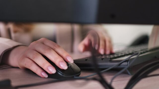Woman works intently on computer keyboard and uses mouse in office. Fingers fly across keys while female employee inputs data into device closeup