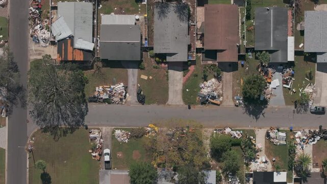 Aerial top-down shot shows rows of houses in St. Petersburg Florida neighborhood with varying degrees of destruction, from piles of trash and debris to roof damage in the wake of Hurricane Milton.