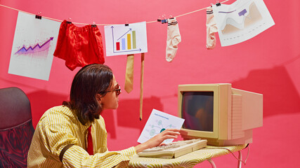 Retro-styled young man sits at ironing desk vintage computer, studying charts and graphs, during...