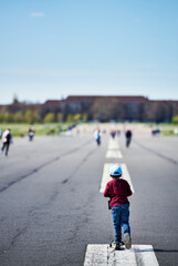 Ready steady go : child riding a scooter on a large airport runway. Kid pretends to take off like an airplane on a airfield tarmac or road conveys a life journey just started. Stamina or speed concept