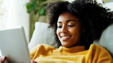 Contented woman looking at digital tablet while sitting on sofa in living room.