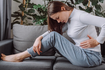Unhealthy sad young woman suffering stomach pain from food poisoning, gastritis and menstrual...