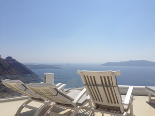 Three reclining chairs with a stunning view of Santorini's turquoise waters, perfect for relaxation