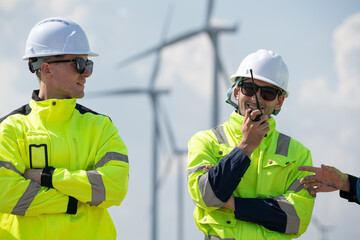 Maintenance engineer team standing at windmills at wind turbine farm. Skill people working outdoors at alternative renewable energy wind power station. Sustainable clean energy technology. Ecology