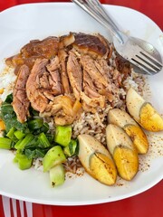 Top view of stewed pork leg on rice with vegetable and boiled egg on wooden background.