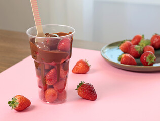 Whole fresh strawberries covered with melted liquid chocolate in cup. Sweet food, dessert on pink...